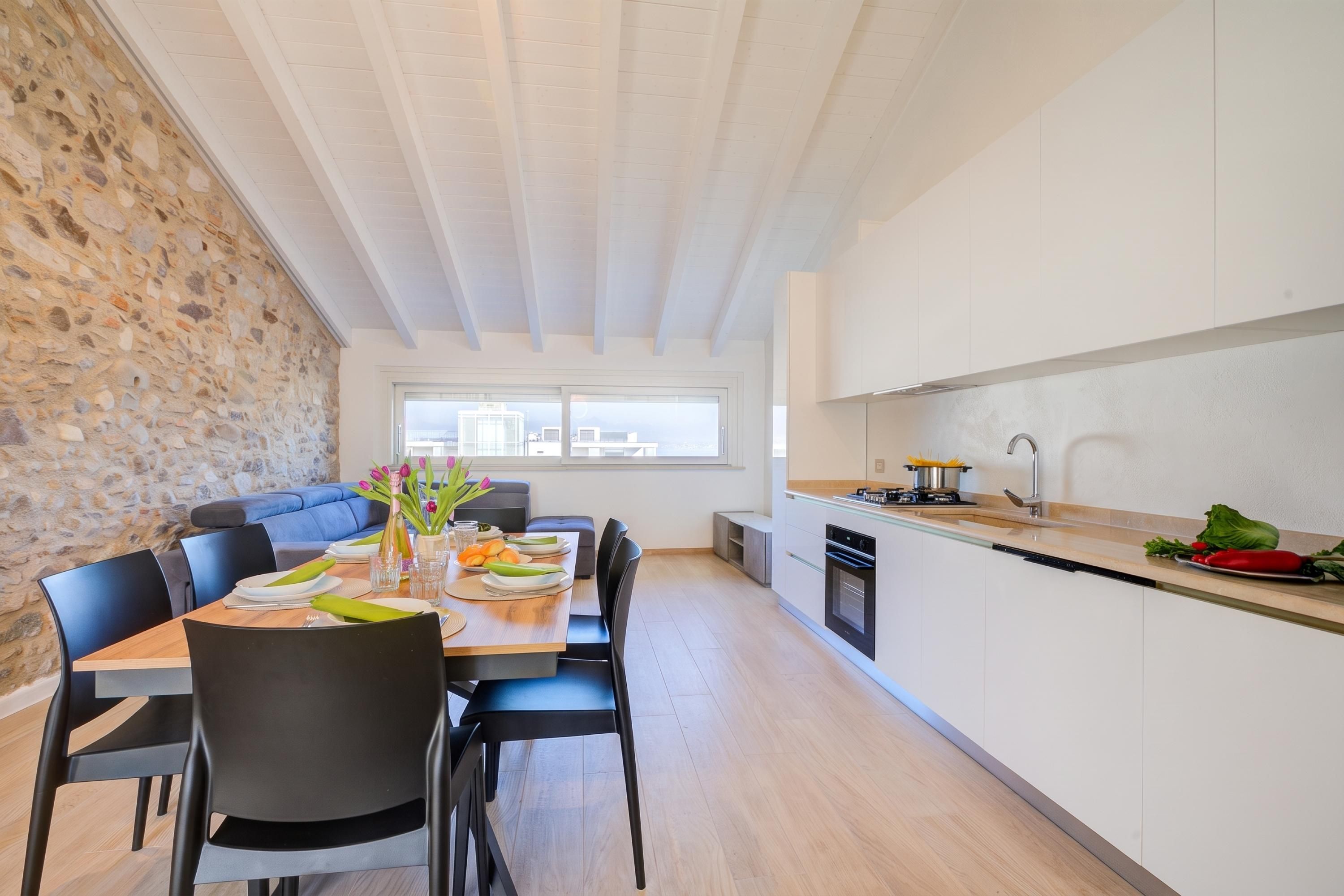 Eine moderne Küche mit Essbereich, Steinwand und großen Fenstern.