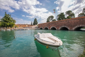 A boat docked in a calm waterway, a bridge in the background, and a clear sky. - Peschiera Apartments Near The Lake (Peschiera del Garda)