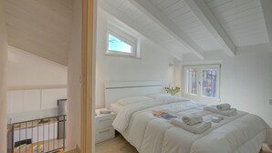 A bedroom with a bed, a nightstand, a window, and a view of the outside.