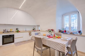 A modern kitchen with white cabinets, a dining table set with plates and glasses, and a window with a view of buildings. - Peschiera Apartments Near The Lake (Peschiera del Garda)
