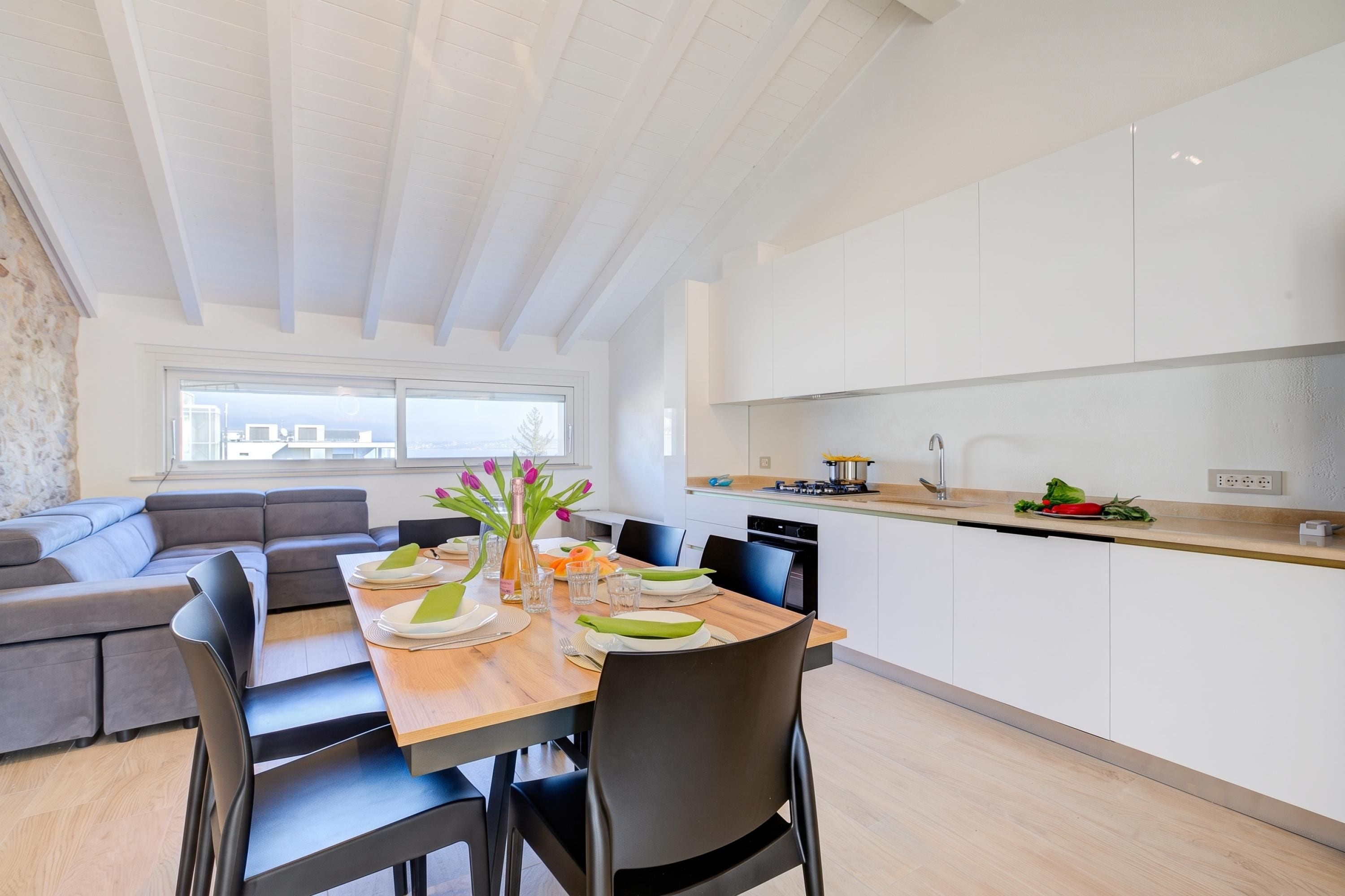 A modern kitchen with white cabinets, a dining table set for four, and a view of the city through large windows.