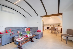 Una sala de estar moderna con un sofá gris, una mesa de centro de madera y una cocina visible a través de un arco.