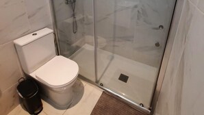 Un baño moderno con ducha de vidrio, inodoro y un cesto de basura.