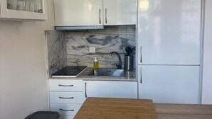 Una cocina moderna con armarios blancos, salpicadero de mármol, encimera de madera y un cubo de basura negro.