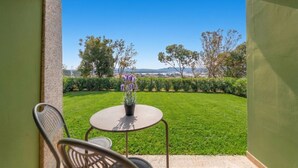 A patio with a table and chairs, a potted plant, and a view of a well-maintained lawn and distant landscape. - Suites Del Borgo (Olbia)