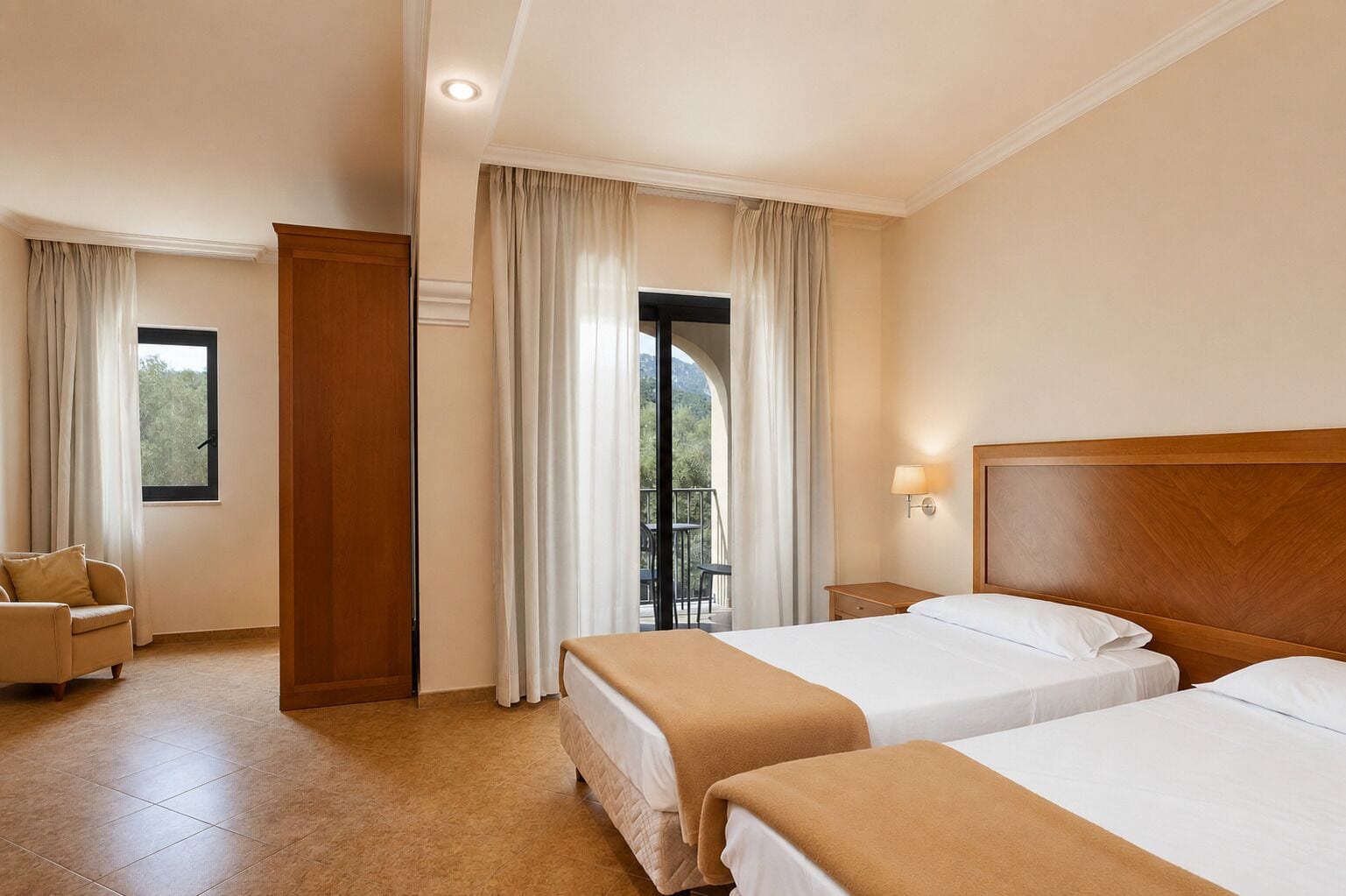 A hotel room with two beds, a sitting area with a chair, a window with curtains, and a balcony view.