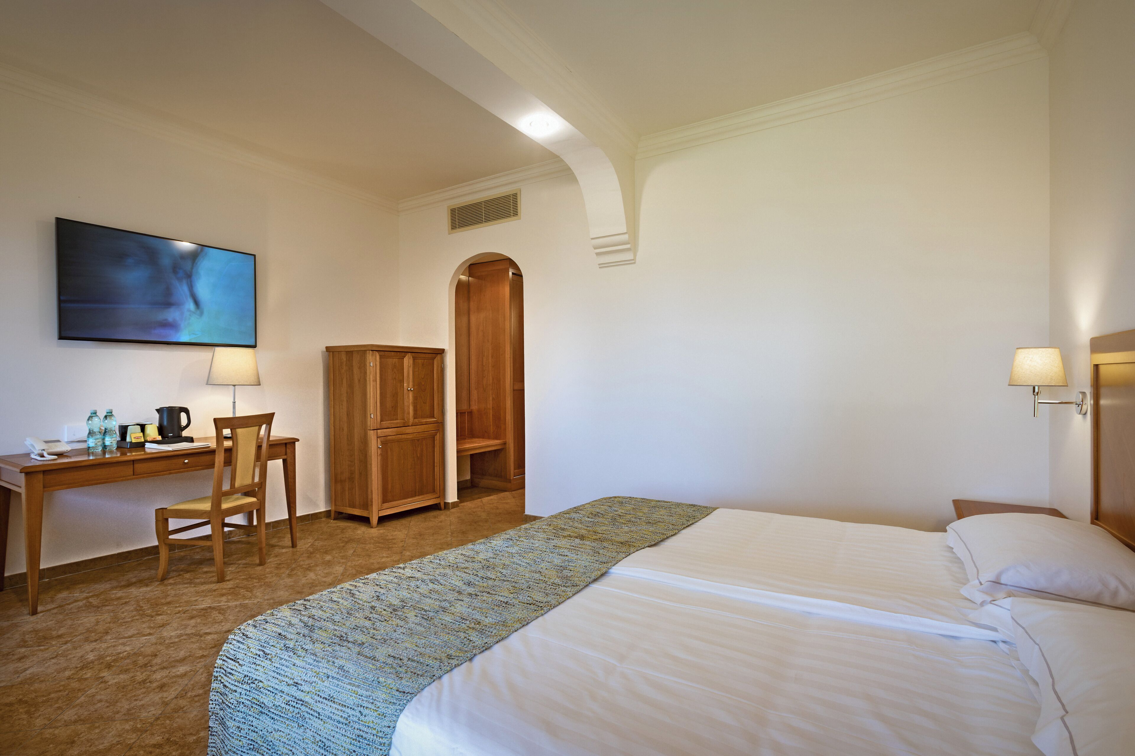 Une chambre d’hôtel avec un lit, un bureau, une chaise, une armoire et un tableau au mur.