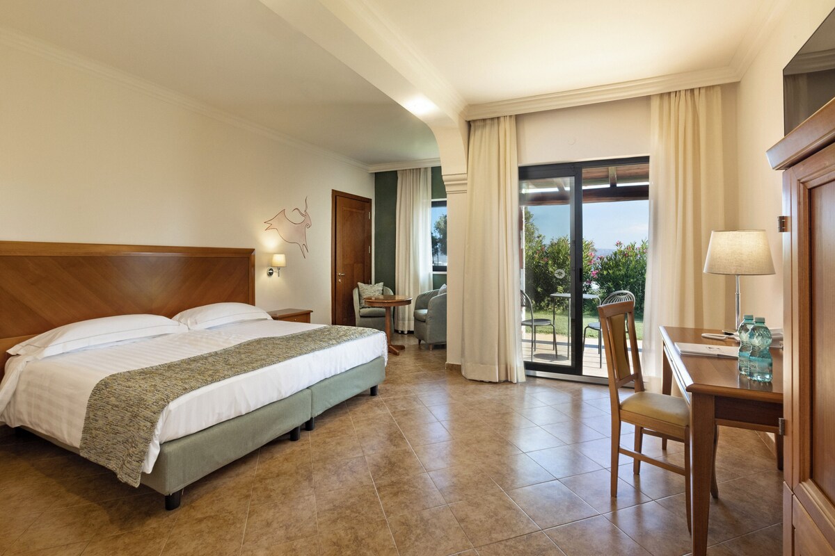 A hotel room with a bed, a desk, a chair, a table, and a view of the outdoors.