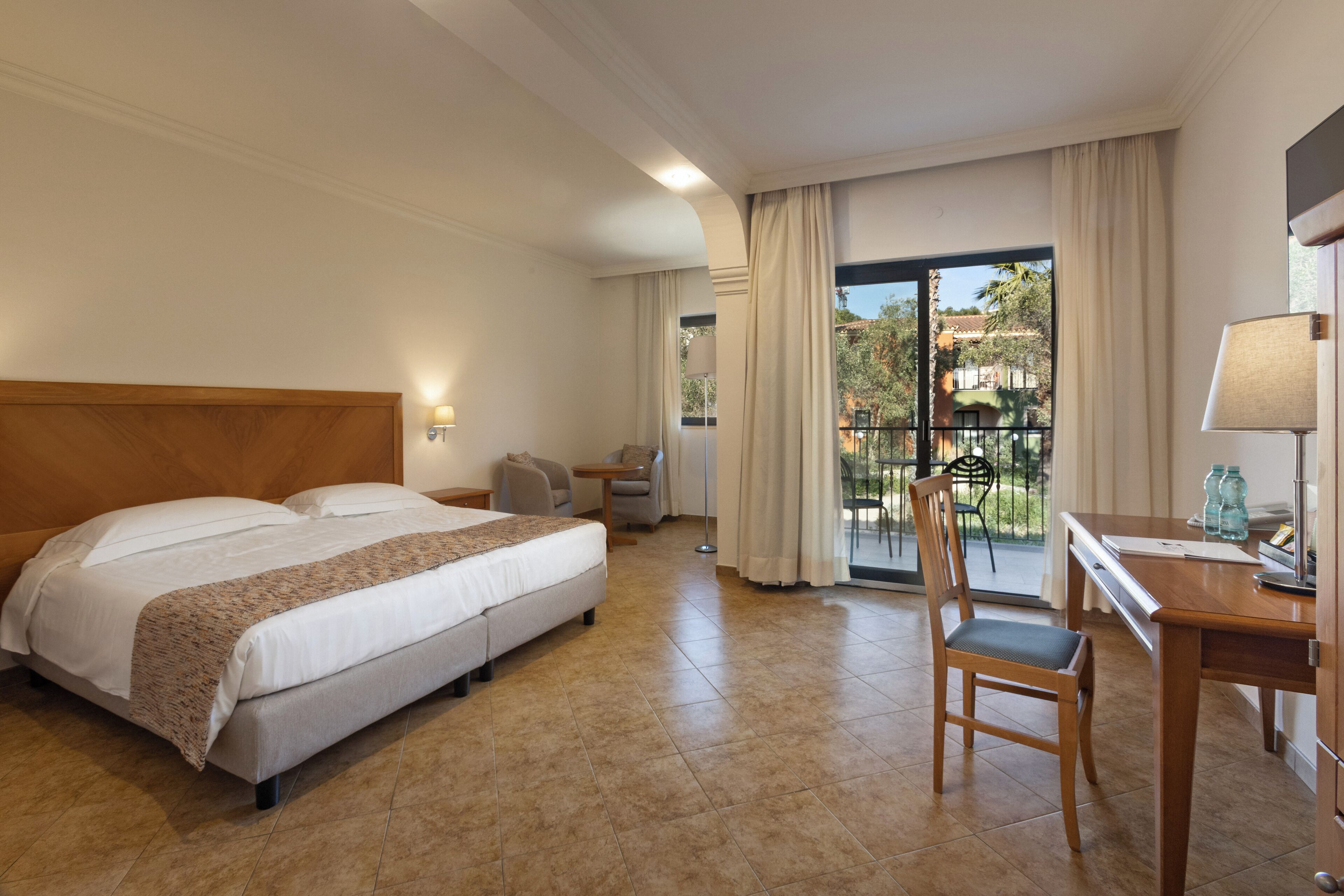 Habitación de hotel con cama, escritorio, silla, mesa y vista al exterior.