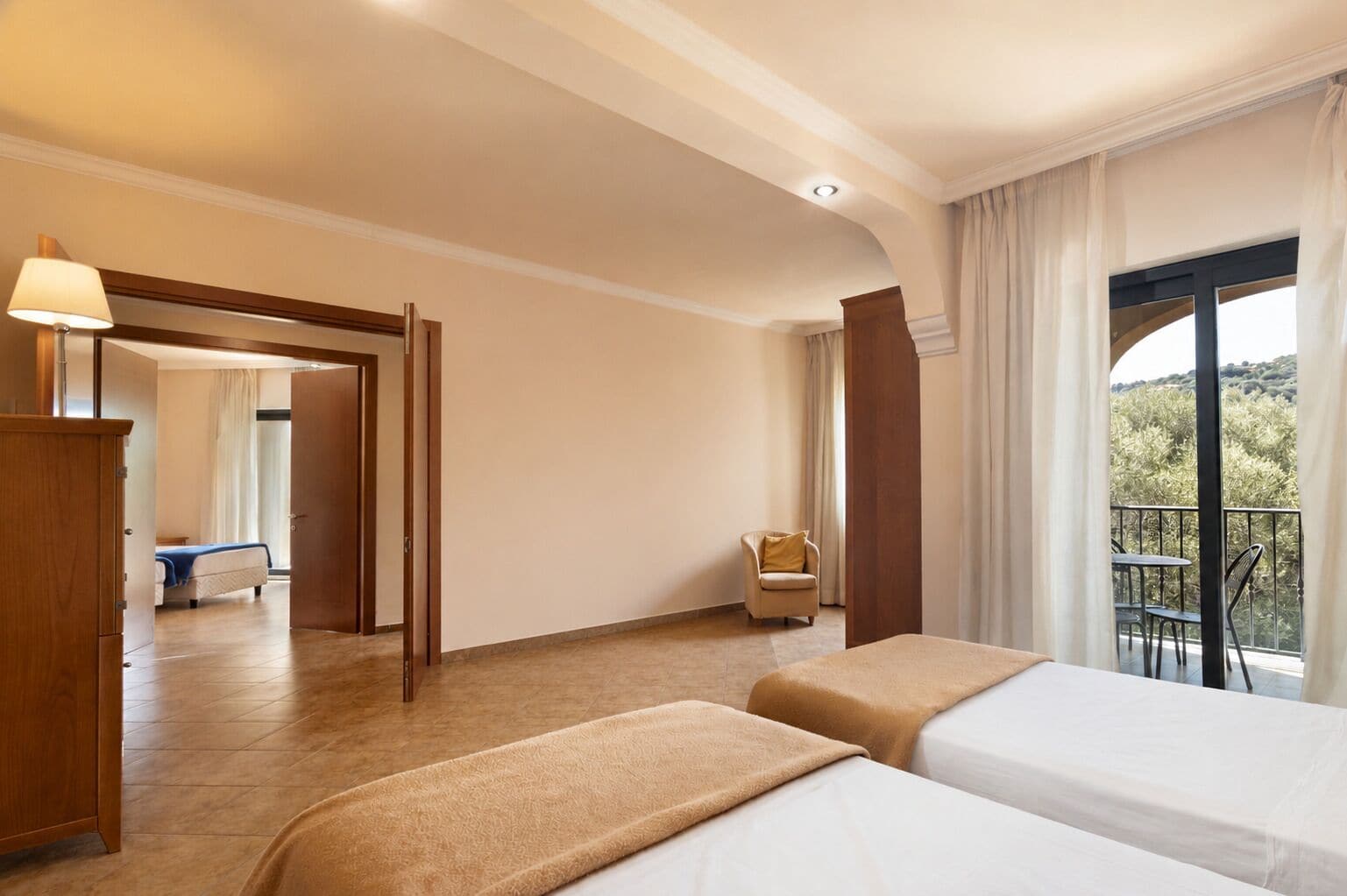 Une chambre d’hôtel avec deux lits, une armoire en bois, une chaise et un balcon avec vue.