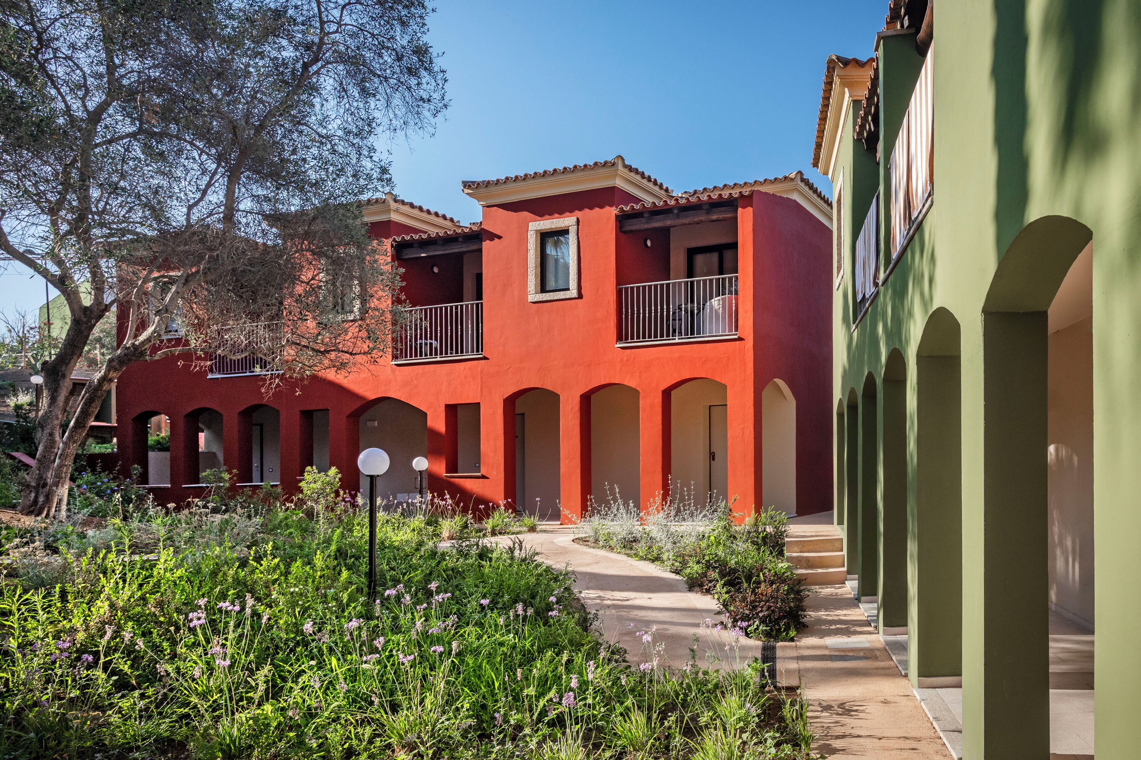 A building with red walls and multiple balconies, surrounded by greenery and a clear sky.