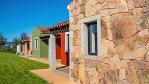 A row of stone-walled buildings with windows, a clear sky, and a well-maintained lawn. - Suites Del Borgo (Olbia)