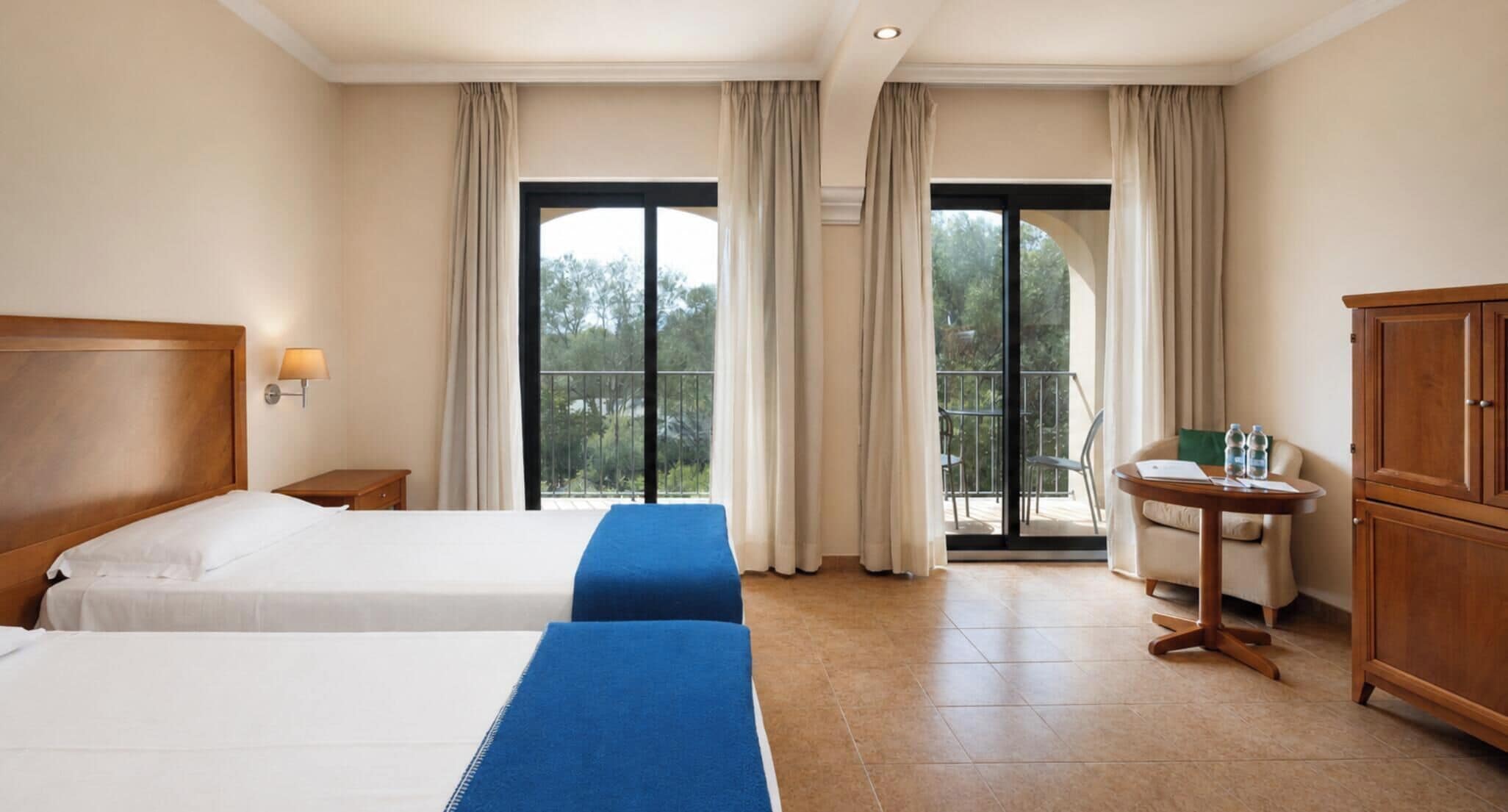 A hotel room with two beds, a balcony, a desk, and a wardrobe.