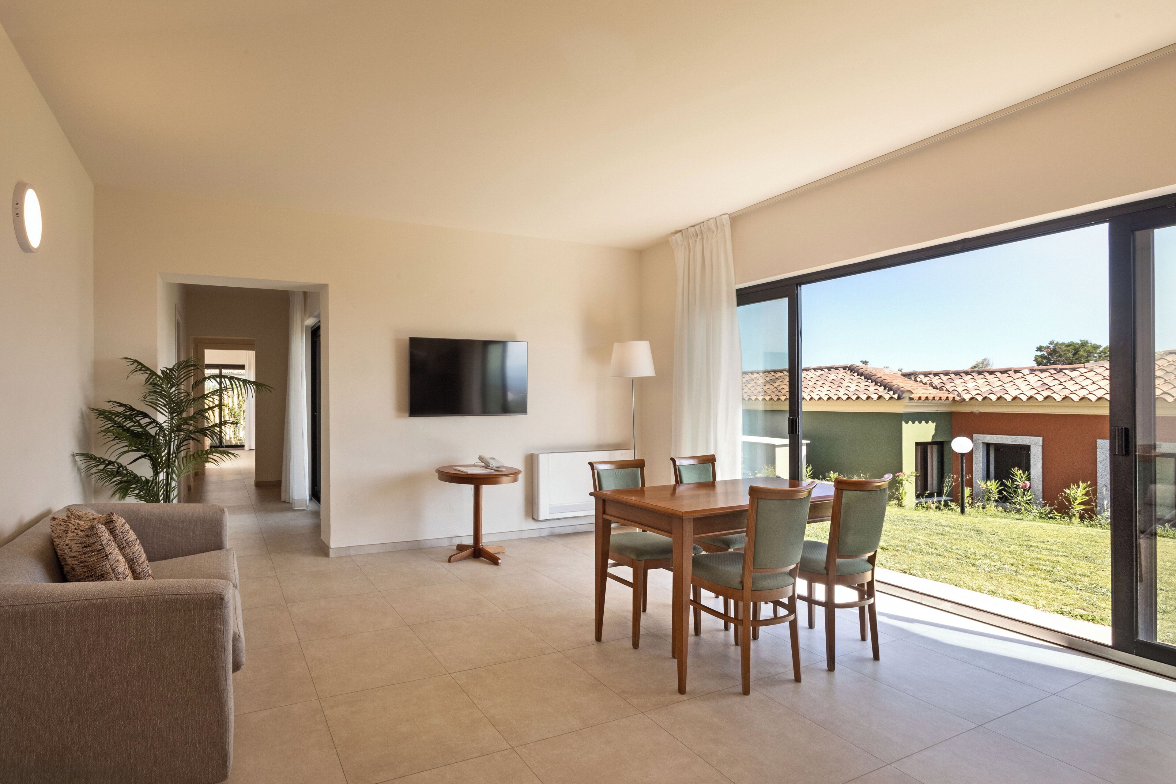A hotel room with a dining area, a sofa, a TV, and a view of the outside.