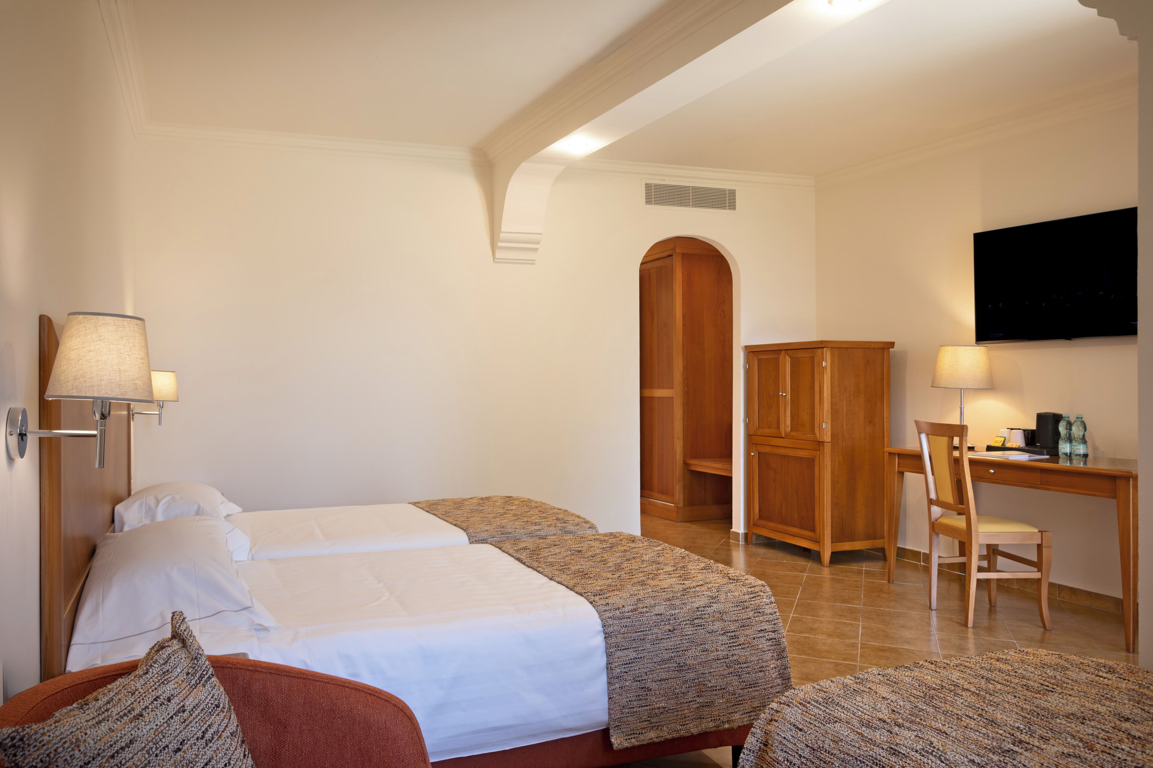 A hotel room with a bed, a desk, a chair, and a television.