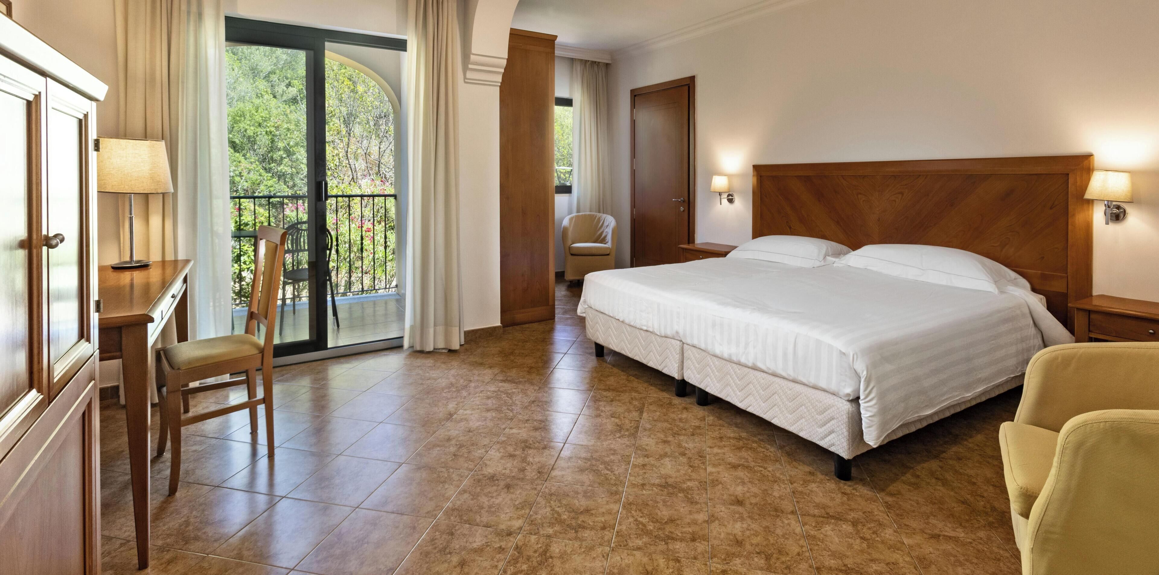 Hotelkamer met een bed, een bureau met stoel, een nachtkastje en uitzicht op groen.