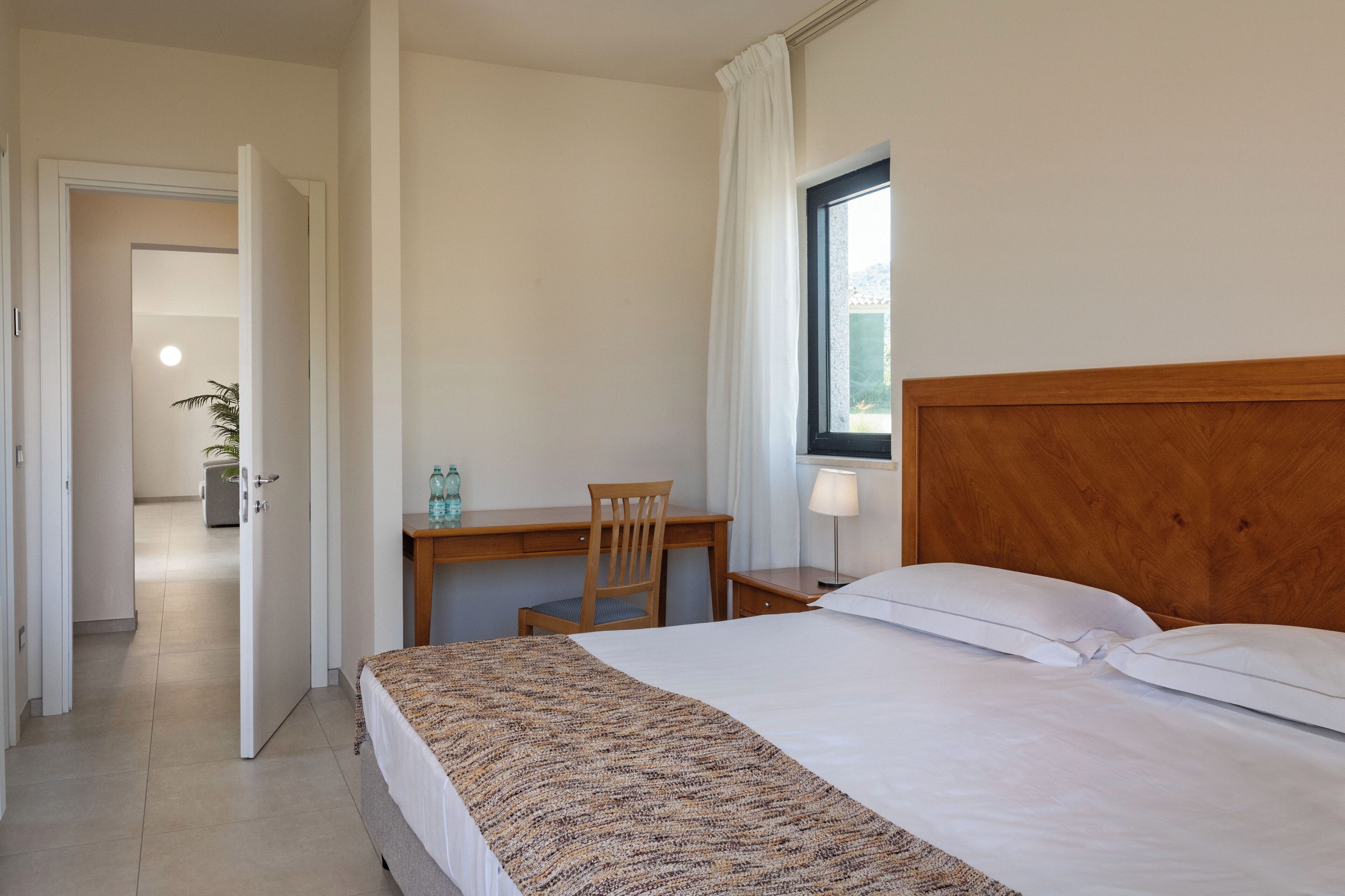 Une chambre d’hôtel avec un lit, un bureau, une chaise, une lampe et une fenêtre.
