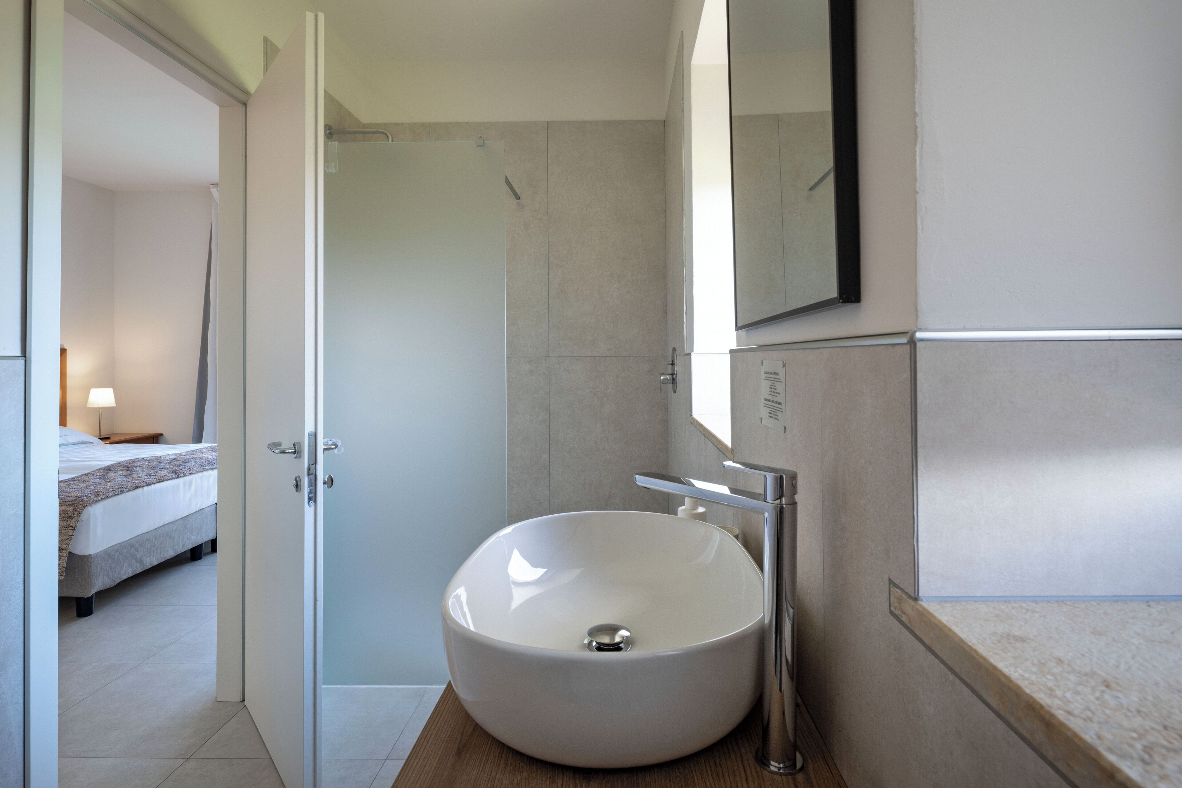 Un bagno moderno con un lavandino bianco grande, uno specchio e uno spazio doccia.