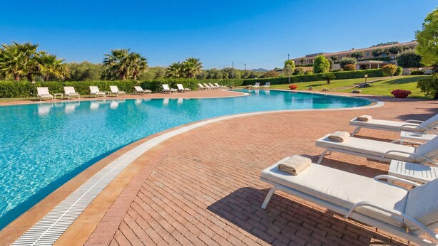 A swimming pool with lounge chairs, a brick deck, and a building in the background. - Suites Del Borgo (Olbia)