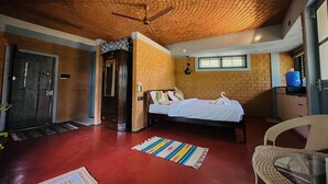 A room with a brick ceiling, a bed with white linens, a wooden door, and a small table with a chair. - Dyavaaprthivi (Shoolagiri)