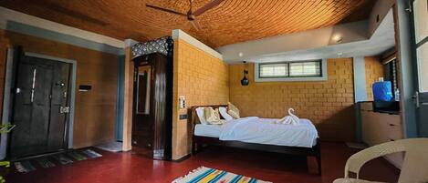 A room with a brick ceiling, a bed with white linens, a wooden door, and a small table with a chair.