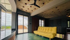 A modern interior with a yellow sofa, large windows, and a unique ceiling design. - Dyavaaprthivi (Shoolagiri)