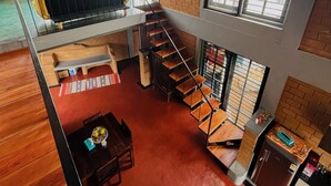 A spacious loft-style apartment with a mezzanine, large windows, a staircase, and a kitchen area. - Dyavaaprthivi (Shoolagiri)