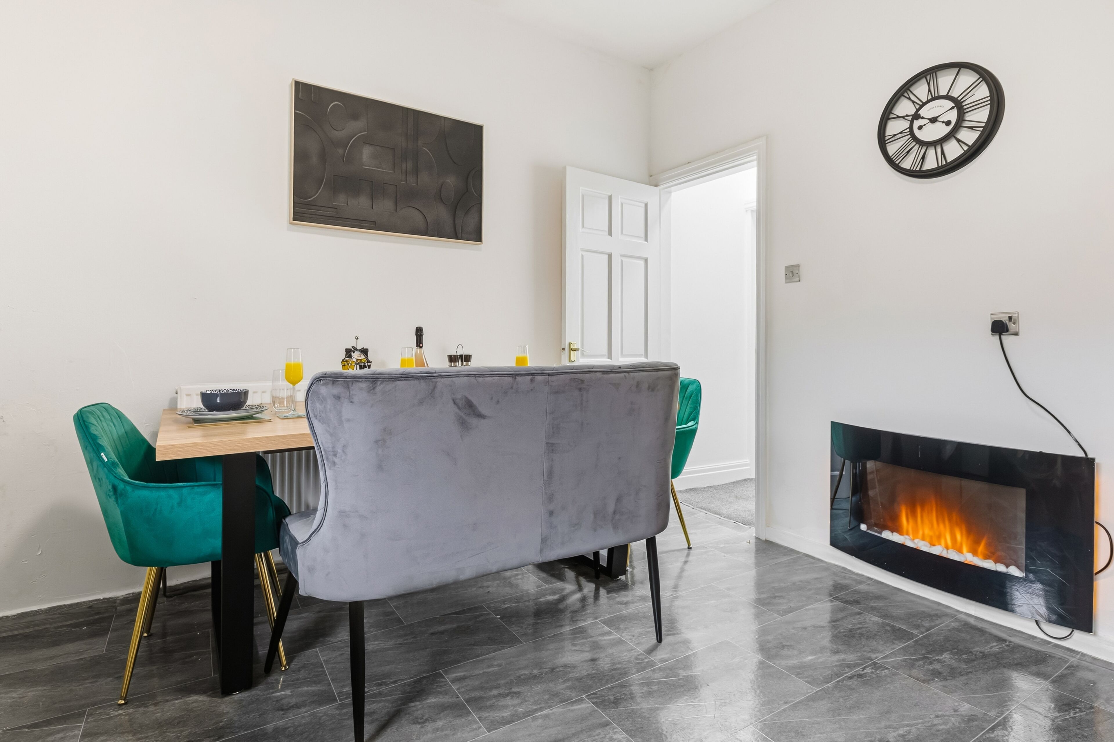A dining area with a table, chairs, a painting, a clock, and a fireplace.