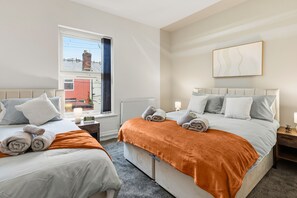 A hotel room with two beds, a window with a view of a building, a radiator, and a wall-mounted artwork. - House - Sleeps 6 - On Street Parking (Manchester)