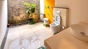 Ein Badezimmer mit Steinwand, Toilette, Waschbecken und Duschbereich.