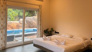 Ein Hotelzimmer mit Bett, Deckenventilator, Klimaanlage, Fenster mit Blick auf einen Pool und einer kleinen Pflanze.