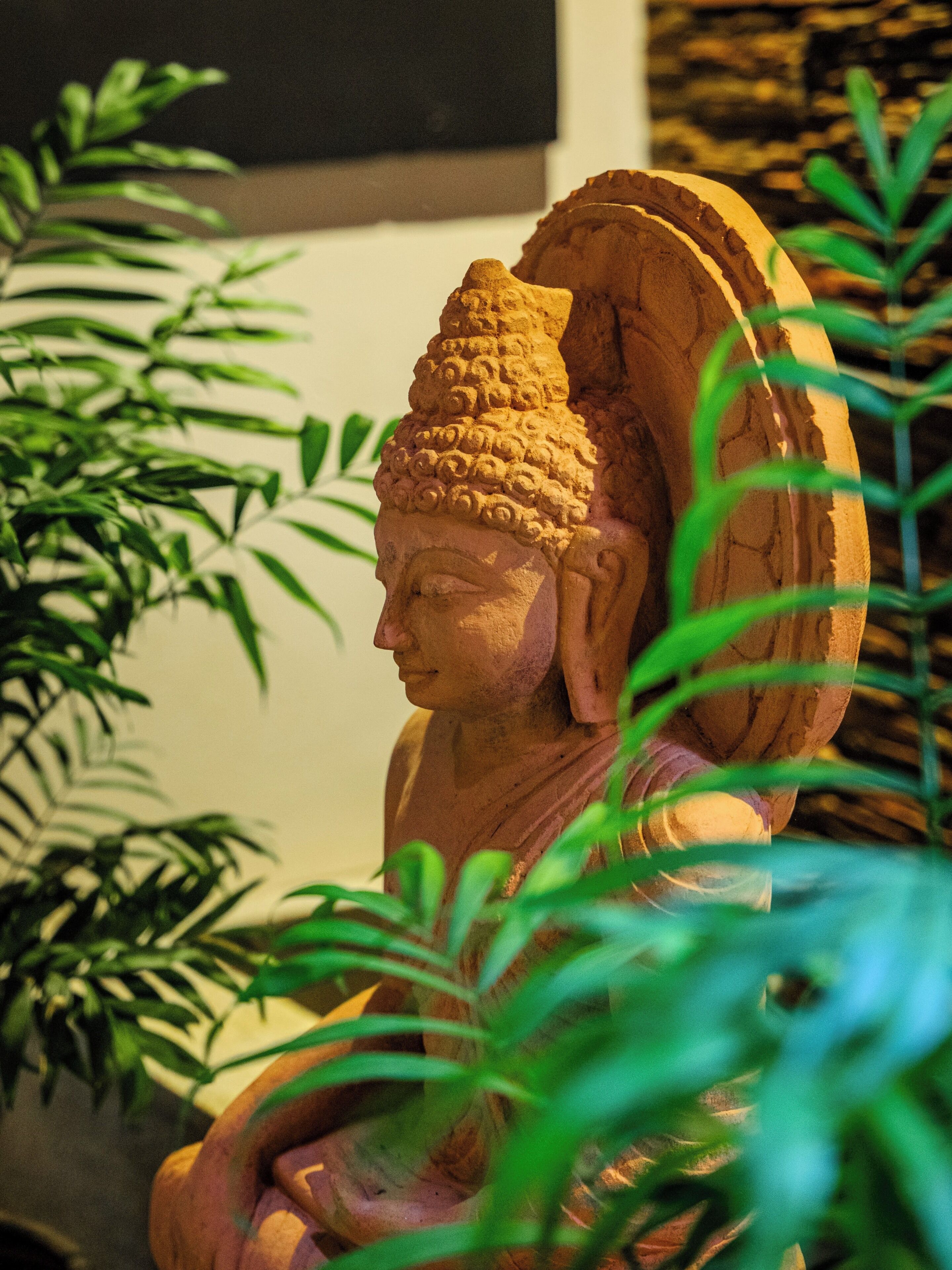 En statue af en siddende figur med vinger, omgivet af vegetation.