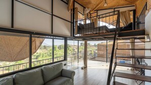 Un'ampia stanza con soffitto alto, un divano, una scala e grandi finestre che si affacciano sul verde.