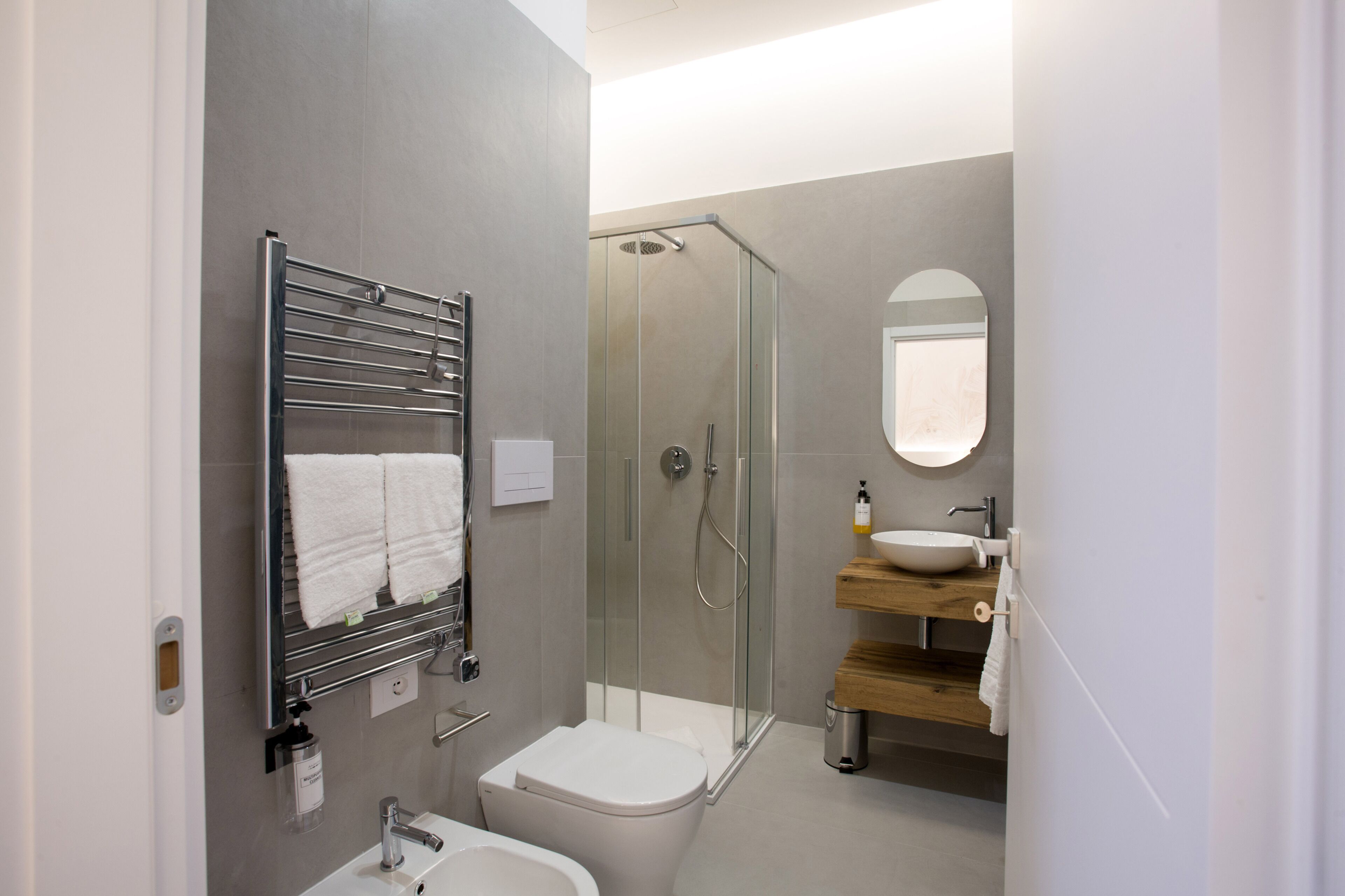 A modern bathroom with a glass-enclosed shower, a white toilet, a sink with a wooden countertop, and a towel rack with two towels.