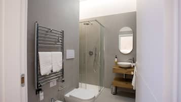 A modern bathroom with a glass-enclosed shower, a white toilet, a sink with a wooden countertop, and a towel rack with two towels.