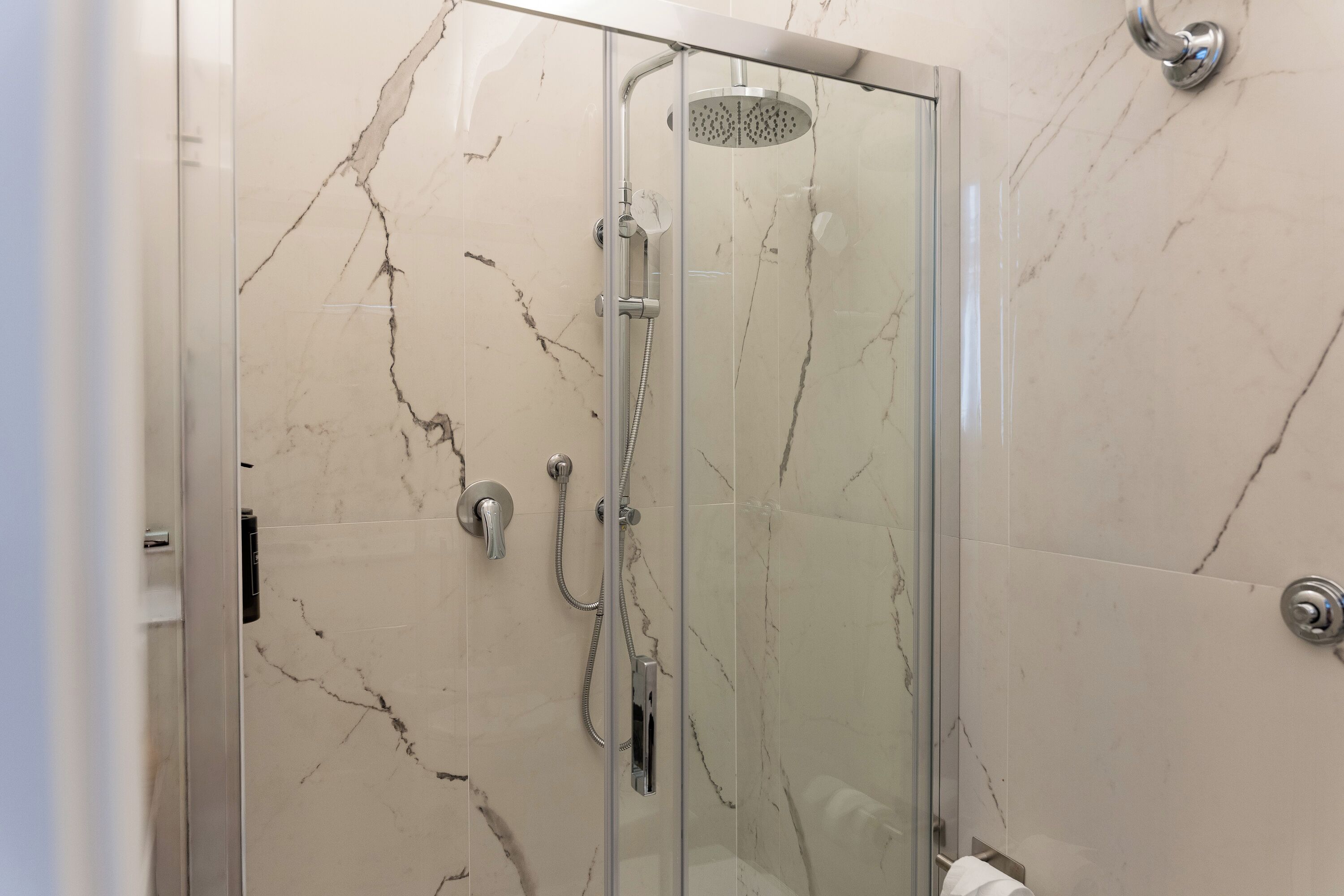 A glass-enclosed shower with a handheld showerhead and a wall-mounted faucet.