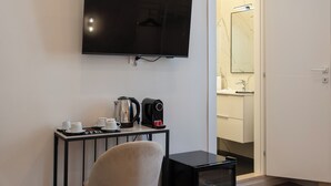 Una camera d'albergo con TV a schermo piatto fissata al muro, un tavolino con bollitore, tazze e tostapane, e una porta che dà sul bagno.
