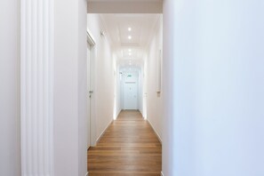 A corridor with white walls and wooden flooring leading to a door marked with the number 6. - Flaminio Collection - Luxury Suites (Rome)