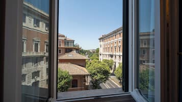 Vista a través de una ventana mostrando una calle con edificios, árboles y un cielo despejado.