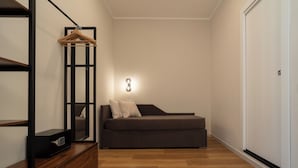 Un dormitorio moderno con sofá cama, cómoda de madera, armario ropero y aplique de pared.