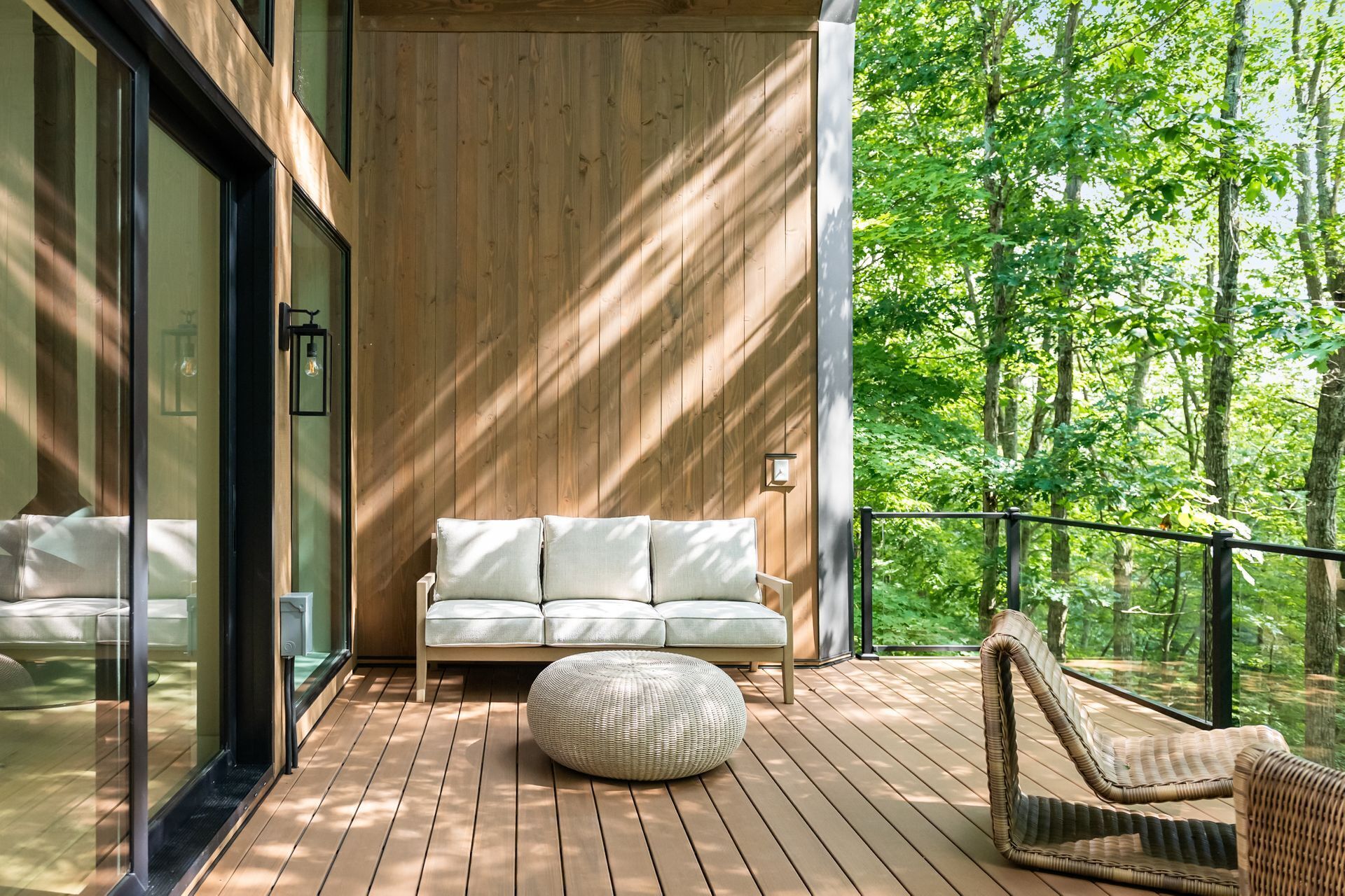 A modern outdoor seating area with a wooden deck, a white sofa, and a wicker chair.