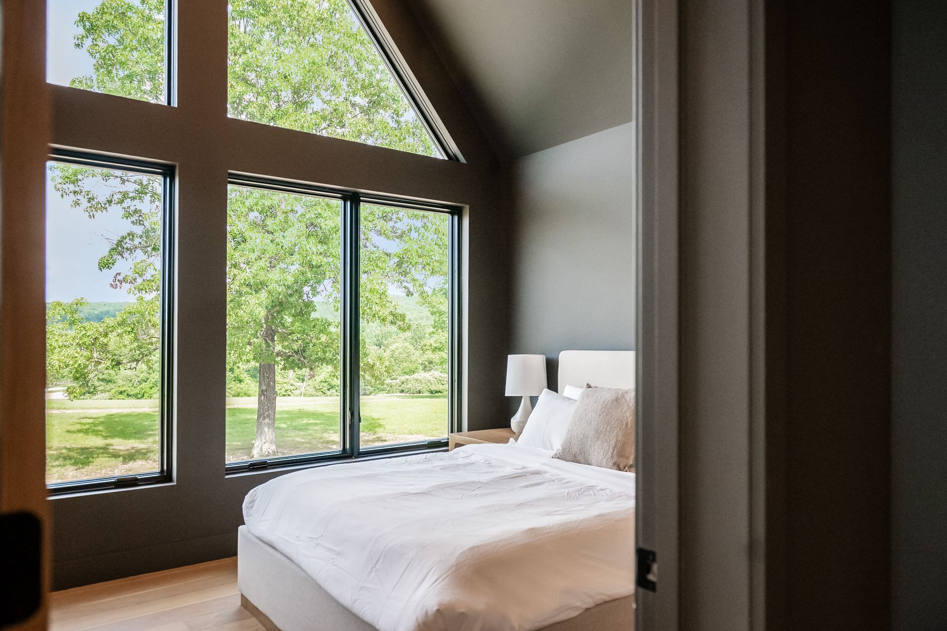 Une chambre avec une grande fenêtre, un lit et une table de chevet.