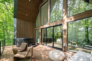 A modern outdoor deck with wicker furniture, a large glass wall, and a view of a forest. - Arcadia Hills - Alpine Ridge (New Plymouth)