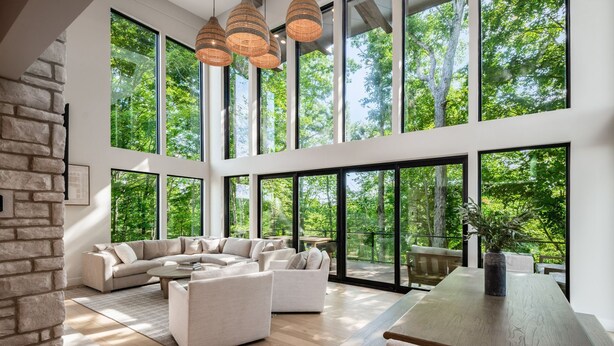 A spacious living area with a large sectional sofa, a wooden dining table, and large windows offering a view of the forest. - Book this Luxury Hocking Hills Lodge! Sleeps 14 (4BR/2.5BA). Enjoy a spa-like bath, full kitchen, fireplace & deck in Arcadia Hills. The ultimate family getaway! (New Plymouth)