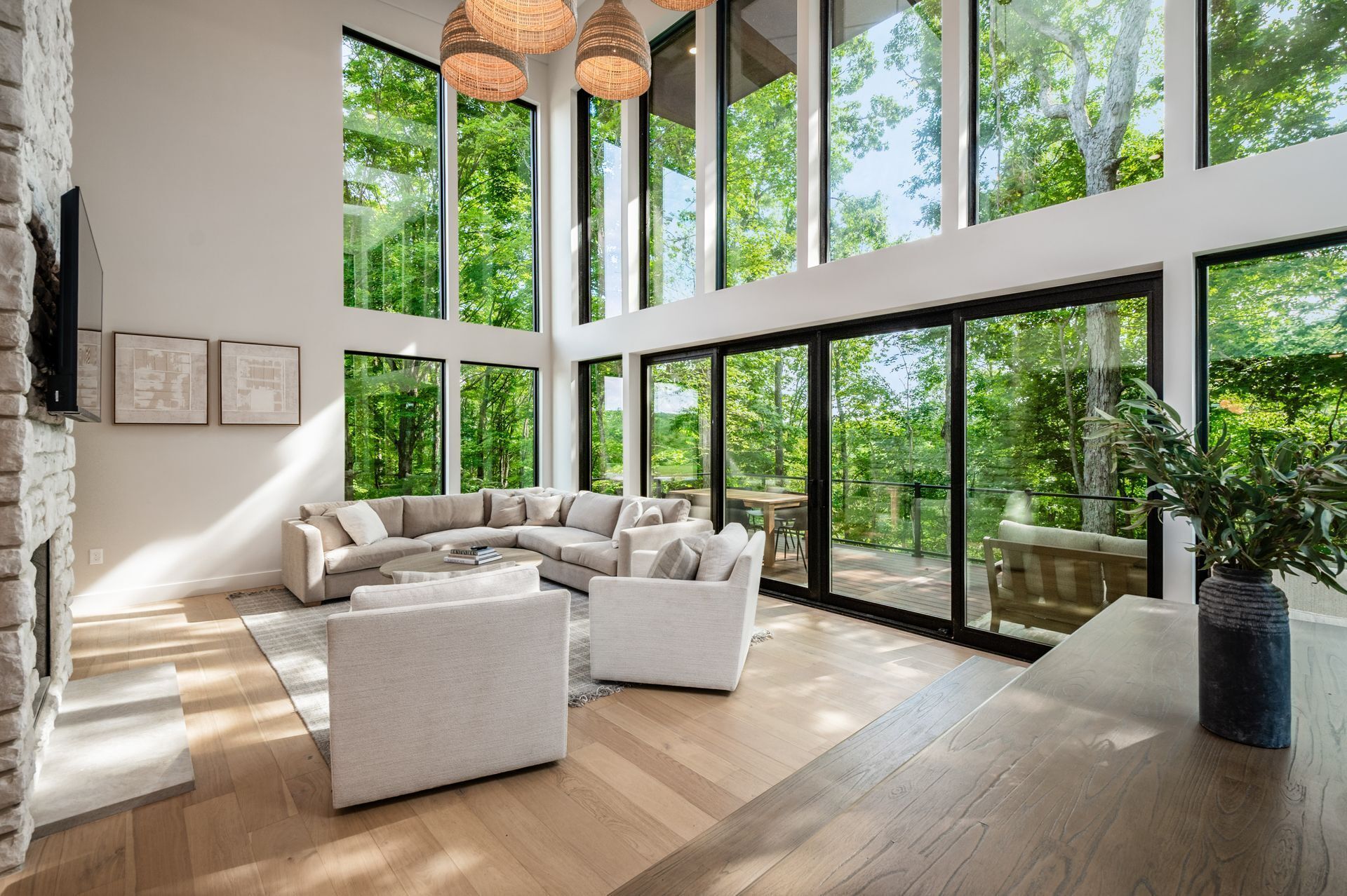 Un vaste espace de vie avec une grande fenêtre donnant sur une forêt, un ensemble de canapés modernes et un plancher en bois.