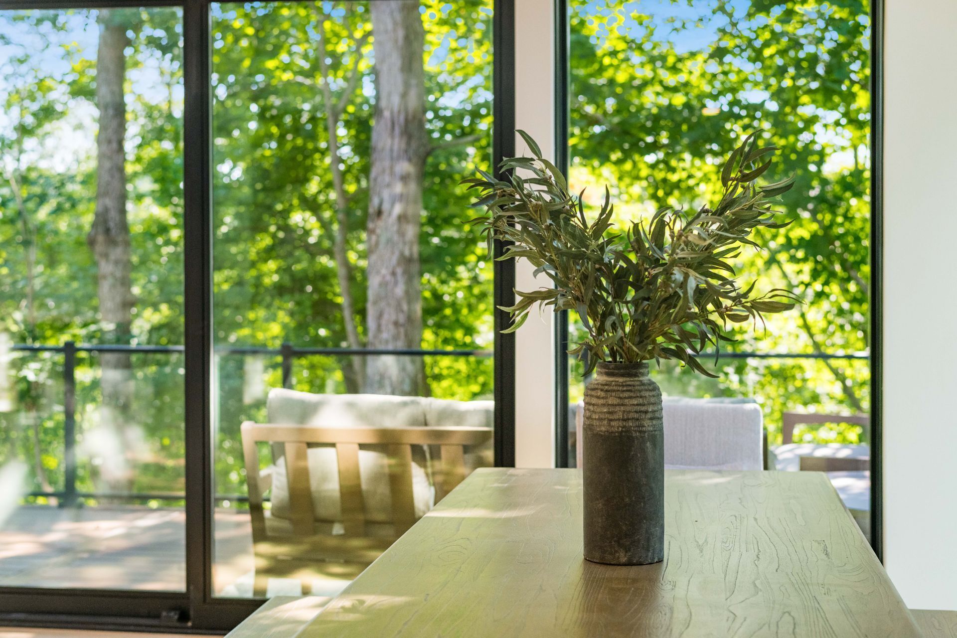 Een kamer met een groot raam, een houten tafel en een vaas met groene planten.