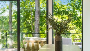 A room with a large window, a wooden table, and a vase with green plants. - Book this Luxury Hocking Hills Lodge! Sleeps 14 (4BR/2.5BA). Enjoy a spa-like bath, full kitchen, fireplace & deck in Arcadia Hills. The ultimate family getaway! (New Plymouth)