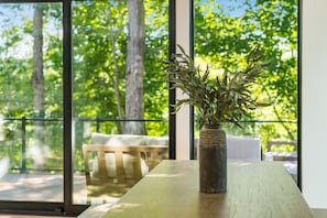 Una habitación con un ventanal grande, una mesa de madera y un florero con plantas verdes.