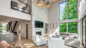 A spacious living area with a stone fireplace, large windows, and a modern staircase. - Book this Luxury Hocking Hills Lodge! Sleeps 14 (4BR/2.5BA). Enjoy a spa-like bath, full kitchen, fireplace & deck in Arcadia Hills. The ultimate family getaway! (New Plymouth)