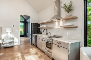 Uma cozinha moderna com eletrodomésticos de aço inoxidável, prateleiras de madeira e vista para o verde.
